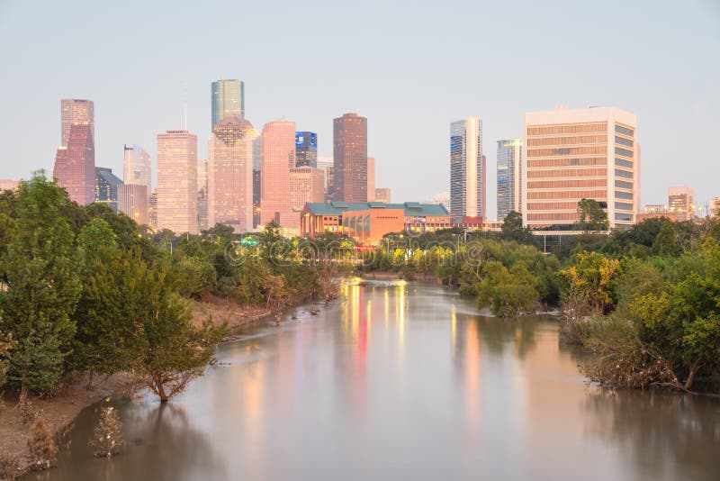 Fast water in Bayou River with downtown Houston, Texas, USA skylines city lights reflection at sunset/twilight. Debris, tree down branches from Hurricane Harvey are spot/available on both river banks. Fast water in Bayou River with downtown Houston, Texas, USA skylines city lights reflection at sunset/twilight. Debris, tree down branches from Hurricane Harvey are spot/available on both river banks