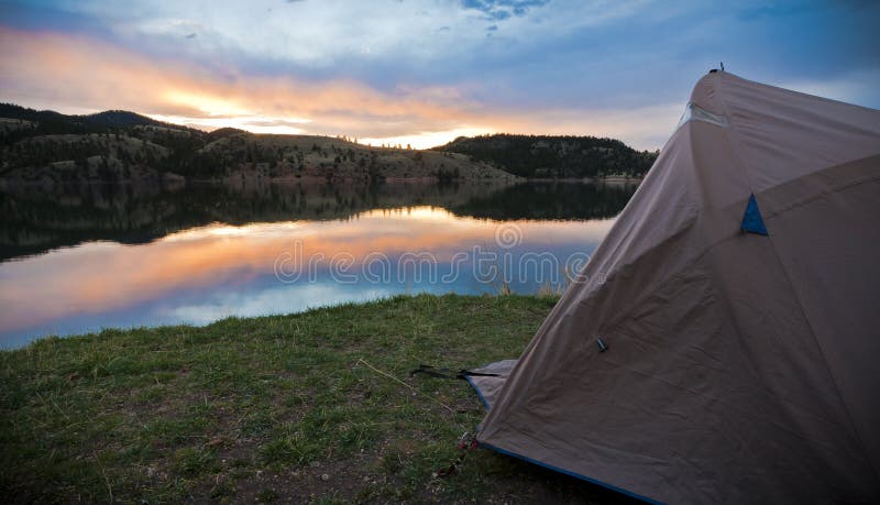 A picture of a tent set up at a mountain lake during a most beautiful sunrise as it reflects on the lake. A picture of a tent set up at a mountain lake during a most beautiful sunrise as it reflects on the lake