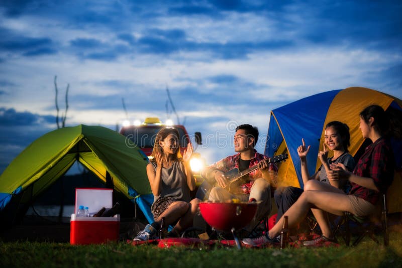 Camping of asian men and women group, relaxing, sing a song and cooking, with ligh from car and tent. Camping of asian men and women group, relaxing, sing a song and cooking, with ligh from car and tent