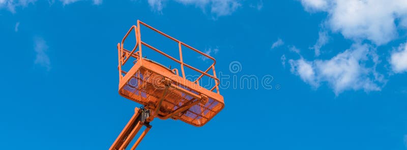 Cherry picker on blue sky background. Boom with lift bucket of heavy machinery. Platform of the telescopic construction lift close-up. Cherry picker on blue sky background. Boom with lift bucket of heavy machinery. Platform of the telescopic construction lift close-up