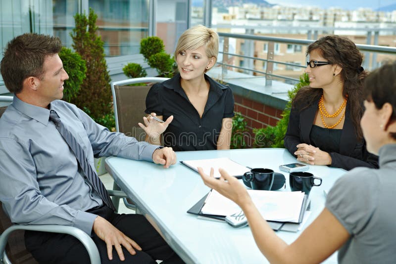 Group of young business people sitting around table on office terrace outdoor, talking and working together. Group of young business people sitting around table on office terrace outdoor, talking and working together.