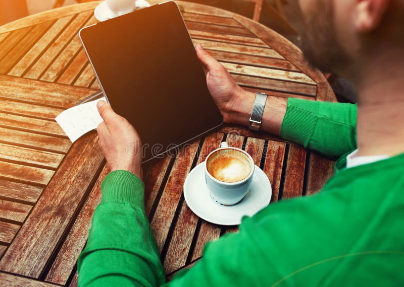 Συνεδρίαση ατόμων στον πίνακα με το φλιτζάνι του καφέ χρησιμοποιώντας την ταμπλέτα οθόνης αφής με την κενή οθόνη στοκ εικόνες με δικαίωμα ελεύθερης χρήσης Συνεδρίαση ατόμων στον πίνακα με το φλιτζάνι του καφέ χρησιμοποιώντας την ταμπλέτα οθόνης αφής με την κενή οθόνη στοκ εικόνες με δικαίωμα ελεύθερης χρήσης