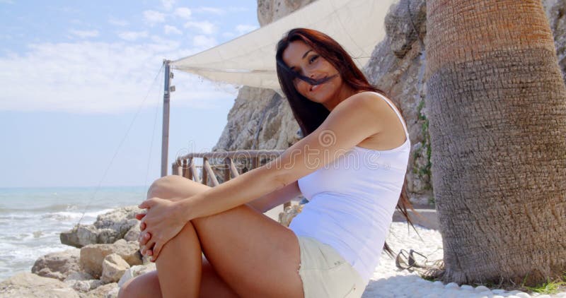Συνεδρίαση γυναικών Brunette στον πέτρινο τοίχο από τον ωκεανό φιλμ μικρού μήκους