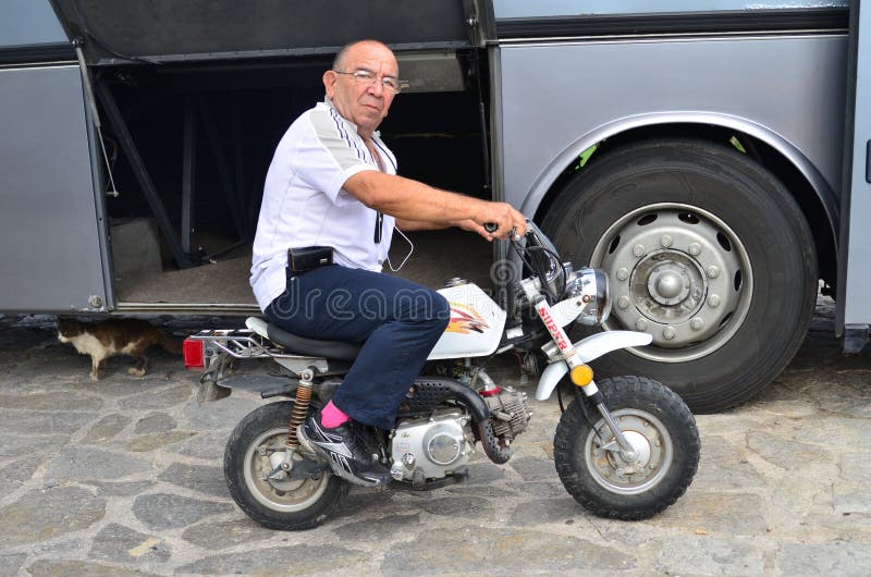 Lefkada, Greece, October 03, 2014: A bus driver is sitting on a very small moped preparing to departure, looking at camera. Lefkada, Greece, October 03, 2014: A bus driver is sitting on a very small moped preparing to departure, looking at camera