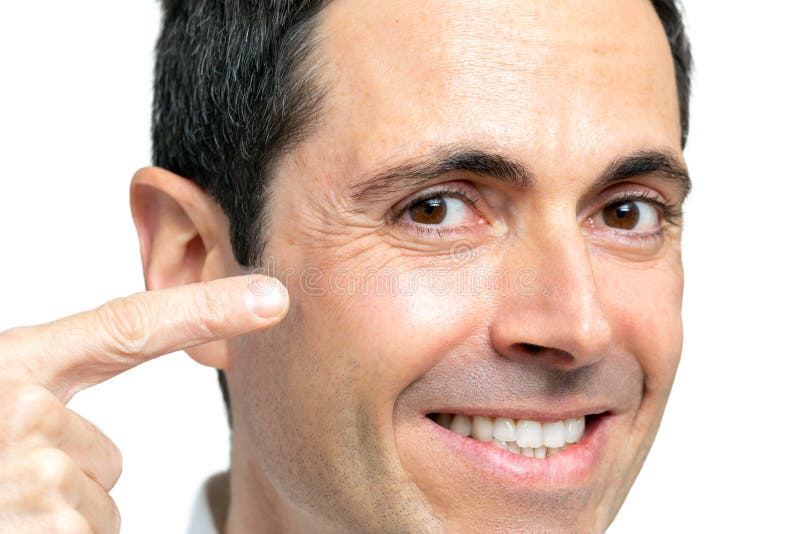 Close up studio portrait of middle age man pointing with finger at crow`s feet next to eye. Isolated on white background. Close up studio portrait of middle age man pointing with finger at crow`s feet next to eye. Isolated on white background