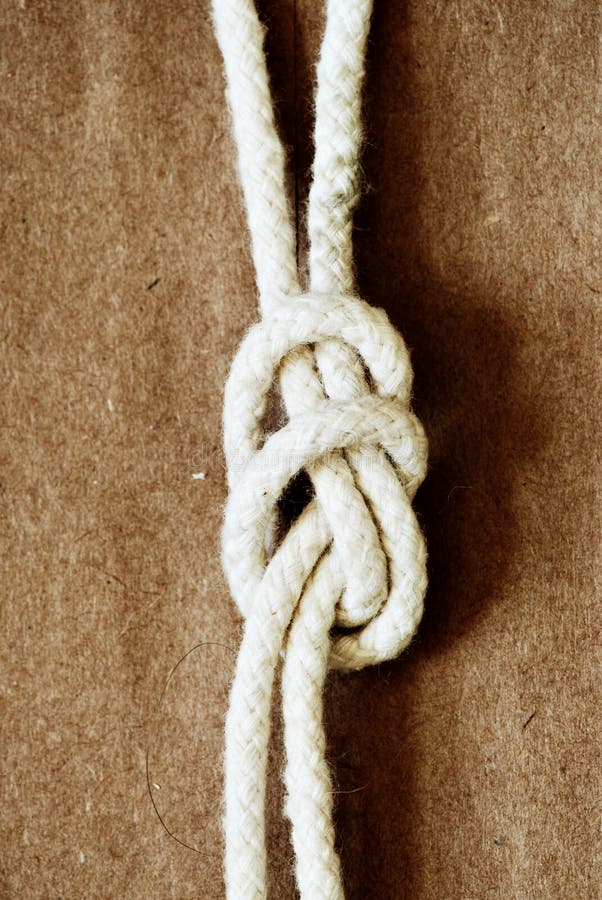 Details of a white rope, tied in a knot on a brownish background. Details of a white rope, tied in a knot on a brownish background.