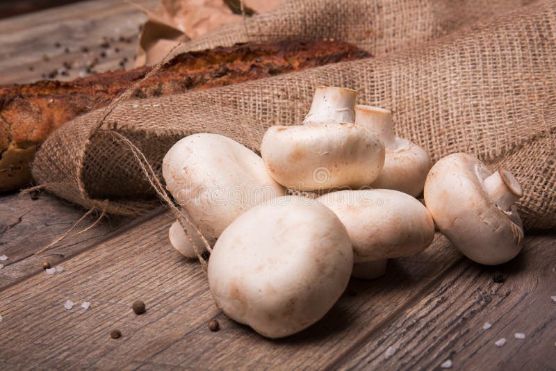 Σωρός ακατέργαστα άσπρα champignons και ένα φρέσκο ψημένο ψωμί σε ένα καφετί ύφασμα και σε ένα ξύλινο υπόβαθρο η σύνθεση κεριών φ στοκ εικόνες Σωρός ακατέργαστα άσπρα champignons και ένα φρέσκο ψημένο ψωμί σε ένα καφετί ύφασμα και σε ένα ξύλινο υπόβαθρο η σύνθεση κεριών φ στοκ εικόνες