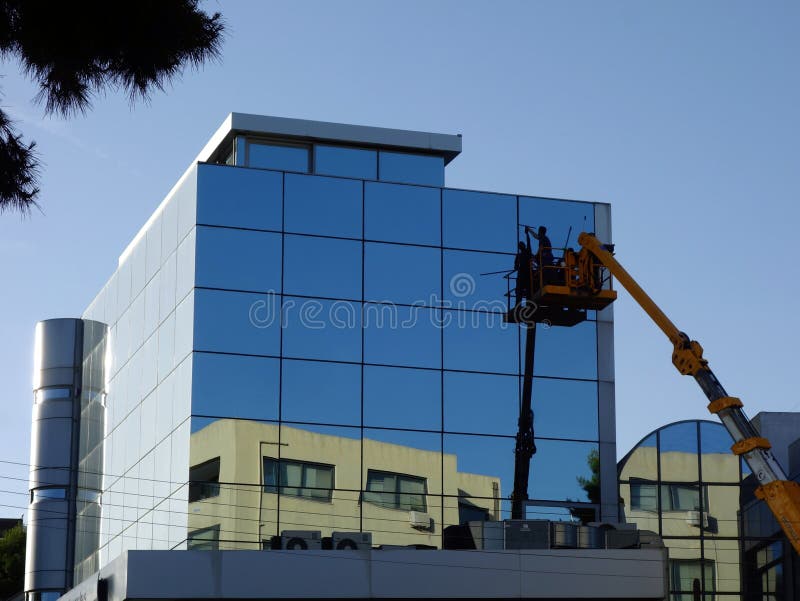 Window cleaning the glass facade of a modern commercial building using a cherry picker mobile lift. Window cleaning the glass facade of a modern commercial building using a cherry picker mobile lift.