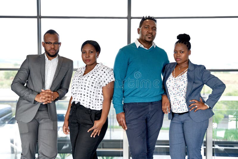 Successful and professional black businessmen and businesswomen waiting in bright location near window looking at camera wearing fashionable corporate clothing. Successful and professional black businessmen and businesswomen waiting in bright location near window looking at camera wearing fashionable corporate clothing