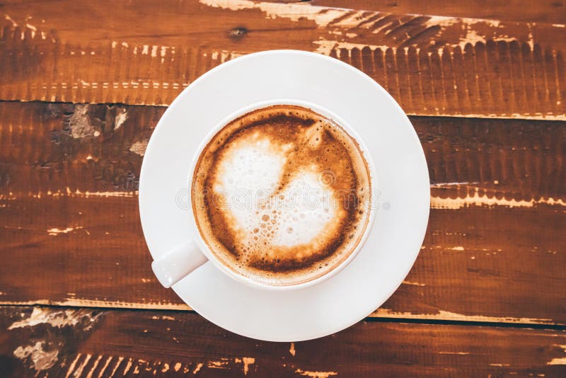Τέχνη μορφής καρδιών latte στο άσπρο φλυτζάνι καφέ στον ξύλινο πίνακα στοκ εικόνες Τέχνη μορφής καρδιών latte στο άσπρο φλυτζάνι καφέ στον ξύλινο πίνακα στοκ εικόνες