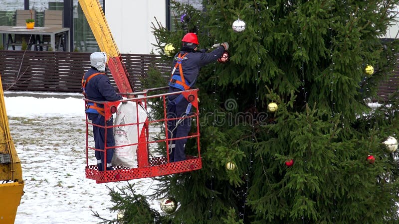 Τα άτομα στο γερανό κρεμούν τα μεγάλα ζωηρόχρωμα παιχνίδια σφαιρών στο υπαίθριο χριστουγεννιάτικο δέντρο