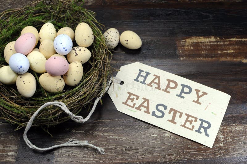 Happy Easter candy easter eggs in birds nest on dark vintage recycled wood background with Happy Easter gift tag sign message greeting. Happy Easter candy easter eggs in birds nest on dark vintage recycled wood background with Happy Easter gift tag sign message greeting.