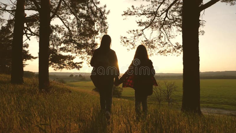 Τα κορίτσια ταξιδεύουν χέρι-χέρι περνούν από το δάσος στο ηλιοβασίλεμα Κορίτσι οδοιπόρων o οι έφηβοι κοριτσιών περπατούν