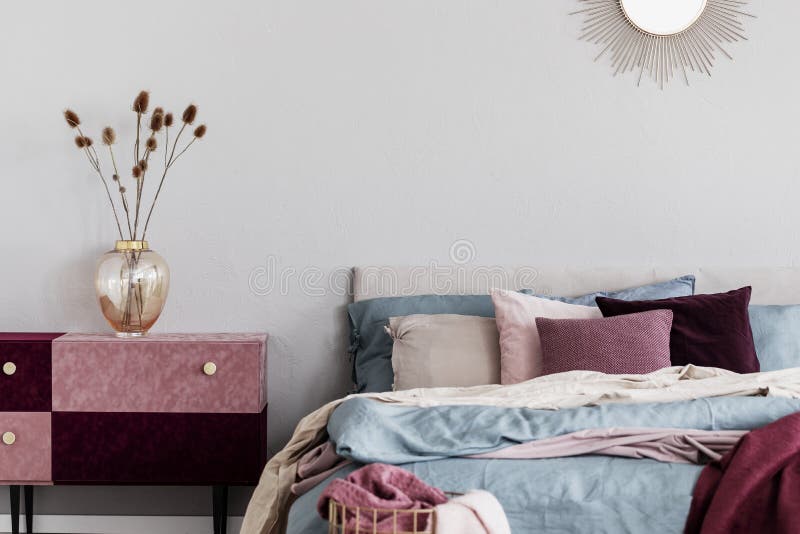 Τα λουλούδια στο κομψό βάζο γυαλιού στο diy βελούδο κάλυψαν το ροζ και burgundy κρητιδογραφιών nightstand δίπλα στο άνετο κρεβάτι στοκ εικόνες