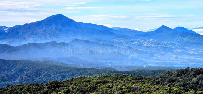 Τα πολυεπίπεδα βουνά και το πράσινο πράσινο δημιουργούν μια συναρπαστική πανοραμική θέα κάτω από έναν γαλάζιο ουρανό στοκ εικόνες