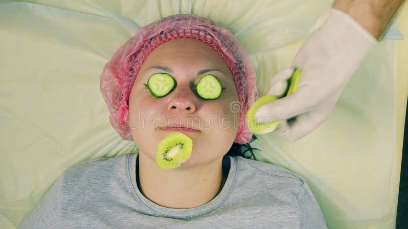 Τα χέρια ενός αρσενικού cosmetologist στα γάντια αφαιρούν από το πρόσωπο μιας γελώντας γυναίκας μια μάσκα του ακτινίδιου
