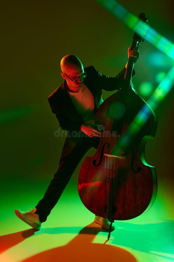 Talented cellist performing jazz compositions in red-green neon light against gradient studio background. Concept of music and art, hobby, concerts and festivals, modern culture. Ad. Talented cellist performing jazz compositions in red-green neon light against gradient studio background. Concept of music and art, hobby, concerts and festivals, modern culture. Ad