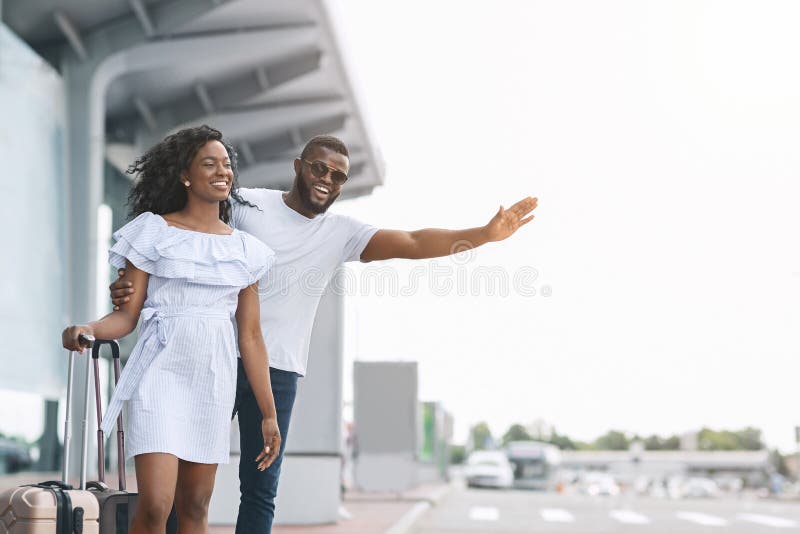 Catching cab. Happy black couple standing at airport parking, man trying to stop taxi with raised hand, copy space. Catching cab. Happy black couple standing at airport parking, man trying to stop taxi with raised hand, copy space