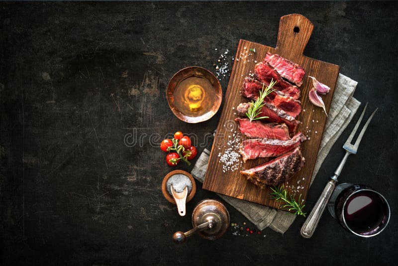 Sliced medium rare grilled beef ribeye steak on cutting board on dark background. Sliced medium rare grilled beef ribeye steak on cutting board on dark background