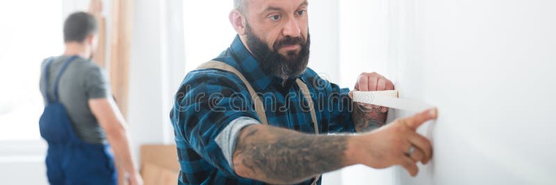 το builder τοποθετεί μια ταινία σε έναν άδειο τοίχο πριν από τη ζωγραφική στοκ φωτογραφία
