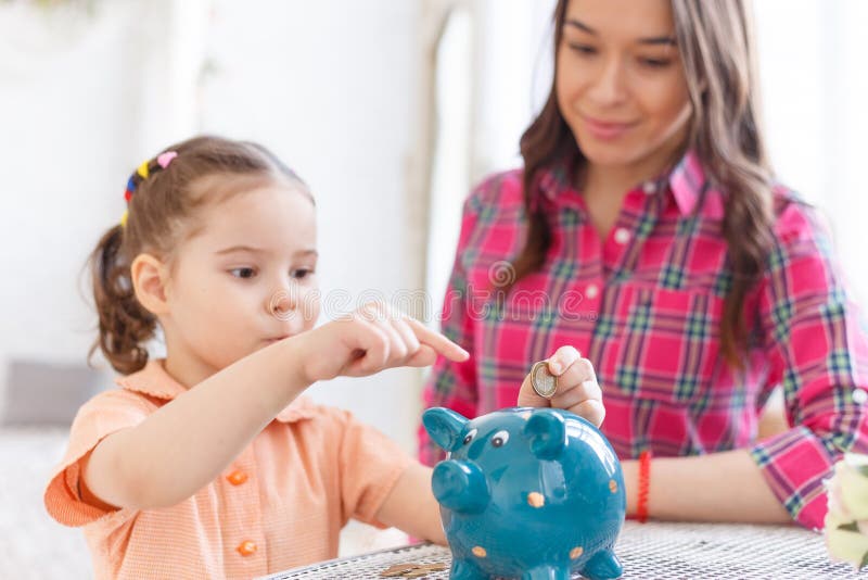 Το Mom διδάσκει μια μικρή κόρη για να συλλέξει τα χρήματα σε μια piggy τράπεζα στοκ φωτογραφία με δικαίωμα ελεύθερης χρήσης Το Mom διδάσκει μια μικρή κόρη για να συλλέξει τα χρήματα σε μια piggy τράπεζα στοκ φωτογραφία με δικαίωμα ελεύθερης χρήσης
