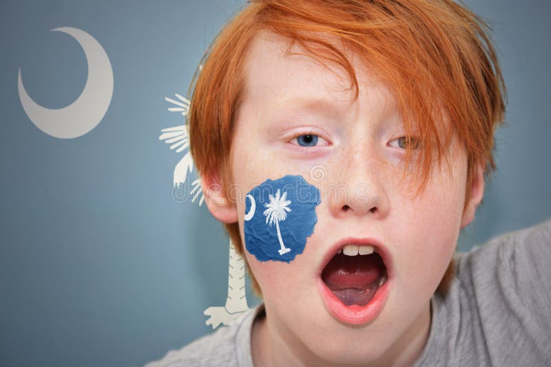Το Redhead αγόρι ανεμιστήρων με την κρατική σημαία της νότιας Καρολίνας χρωμάτισε στο πρόσωπό του στοκ φωτογραφία Το Redhead αγόρι ανεμιστήρων με την κρατική σημαία της νότιας Καρολίνας χρωμάτισε στο πρόσωπό του στοκ φωτογραφία