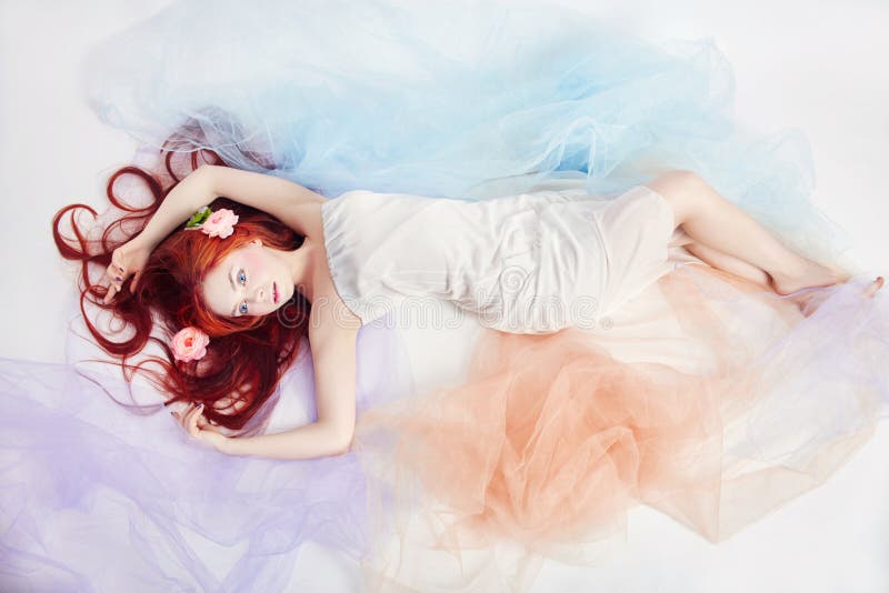 Το Redhead κορίτσι στο ελαφρύ αερώδες χρωματισμένο φόρεμα βρίσκεται στο άσπρο υπόβαθρο πατωμάτων Όμορφα λουλούδια στην τρίχα κορι στοκ εικόνα Το Redhead κορίτσι στο ελαφρύ αερώδες χρωματισμένο φόρεμα βρίσκεται στο άσπρο υπόβαθρο πατωμάτων Όμορφα λουλούδια στην τρίχα κορι στοκ εικόνα