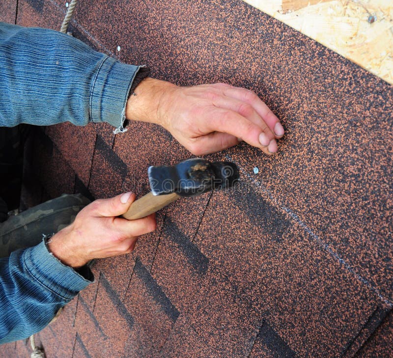 Roofer installs Asphalt Shingles or bitumen roof shingles - closeup on hands. Roofing repair. Roofer installs Asphalt Shingles or bitumen roof shingles - closeup on hands. Roofing repair