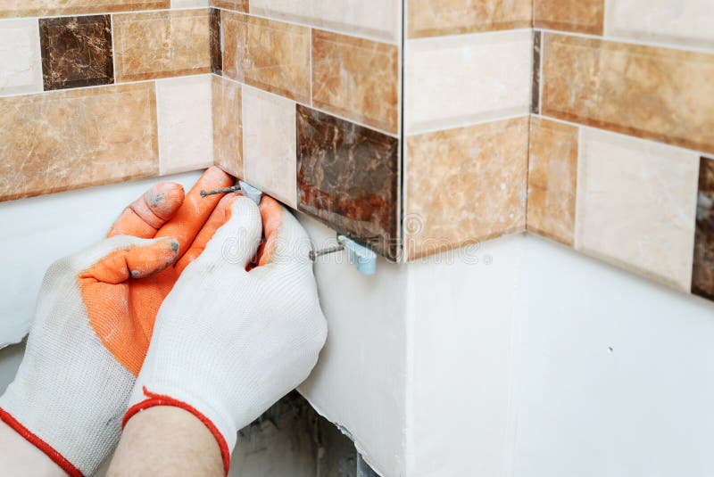 The tiler& x27;s hands are using plastic wedges to align tiles on the wall. The tiler& x27;s hands are using plastic wedges to align tiles on the wall.