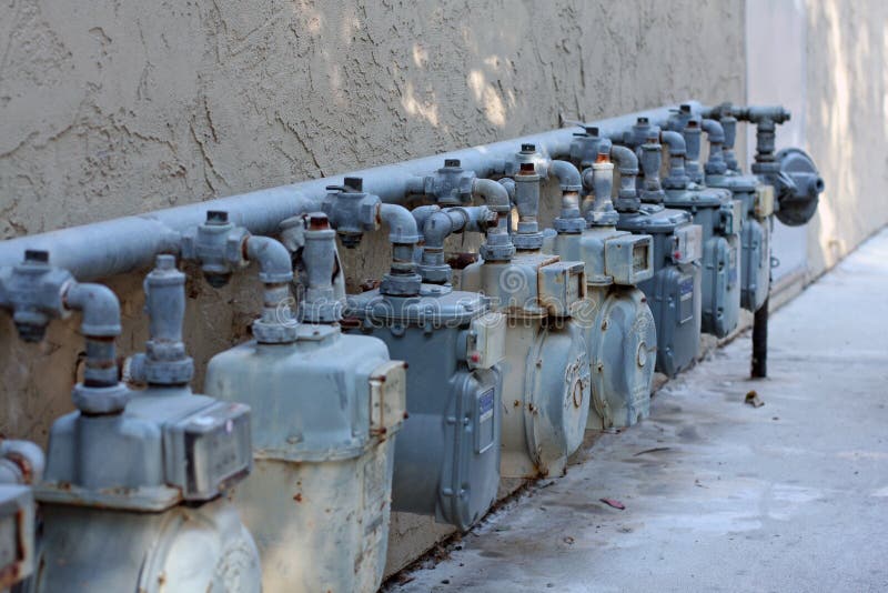 A row of natural gas meters is attached to a stucco building. A row of natural gas meters is attached to a stucco building.