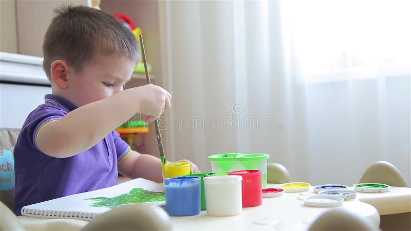 Το αγόρι σύρει με τα χρωματισμένα χρώματα καθμένος στον πίνακα