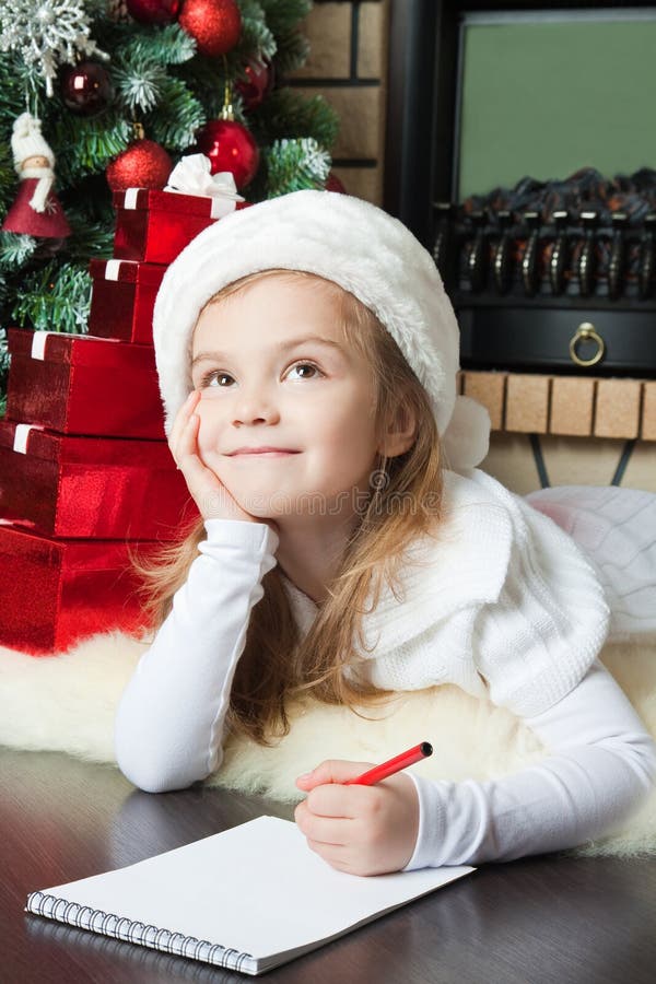 Το αστείο κορίτσι στο καπέλο Santa γράφει την επιστολή σε Santa στοκ φωτογραφίες