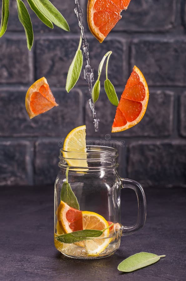 Grapefruit lemon and sage infused water with flying slices on dark background. Grapefruit lemon and sage infused water with flying slices on dark background