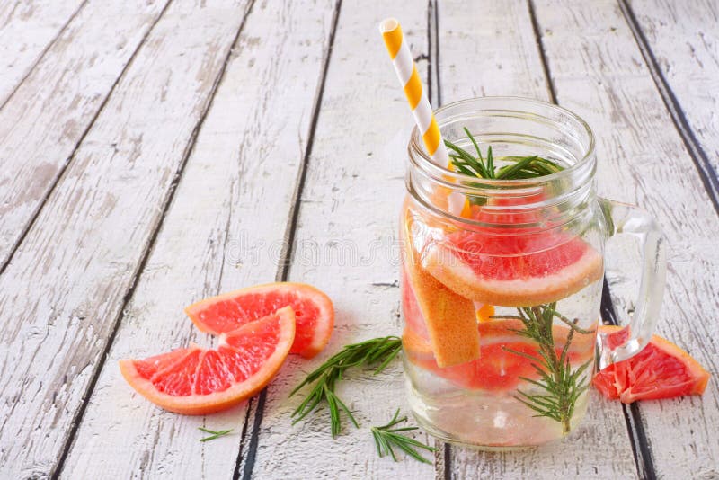 Grapefruit and rosemary infused detox water in a mason jar glass against a rustic white wood background. Grapefruit and rosemary infused detox water in a mason jar glass against a rustic white wood background
