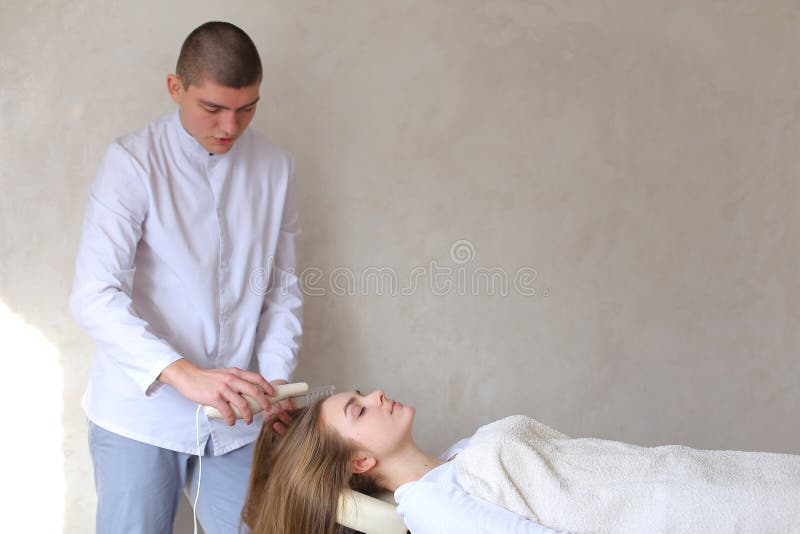Το εντυπωσιακό αρσενικό αρσενικό cosmetologist κάνει το επικεφαλής μασάζ με ειδικό στοκ φωτογραφίες