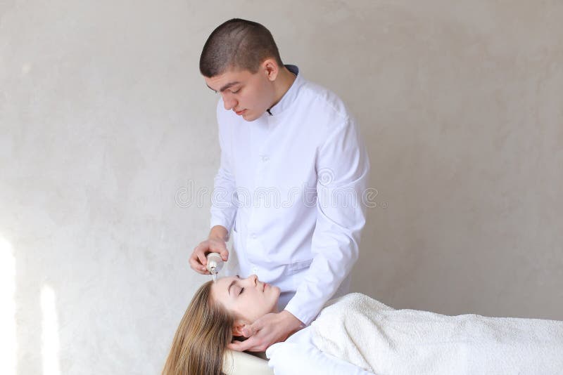 Το εντυπωσιακό αρσενικό αρσενικό cosmetologist κάνει το επικεφαλής μασάζ με ειδικό στοκ φωτογραφίες