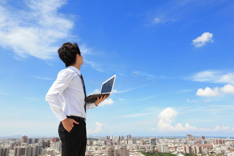 Young business man using laptop and look to blue sky and cloud with cityscape in the background, business and cloud computing concept. Young business man using laptop and look to blue sky and cloud with cityscape in the background, business and cloud computing concept