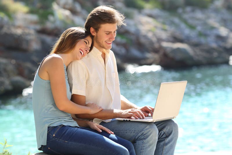 Το ευτυχές ζεύγος χρησιμοποιεί ένα lap-top στις διακοπές στην παραλία στοκ εικόνα με δικαίωμα ελεύθερης χρήσης Το ευτυχές ζεύγος χρησιμοποιεί ένα lap-top στις διακοπές στην παραλία στοκ εικόνα με δικαίωμα ελεύθερης χρήσης