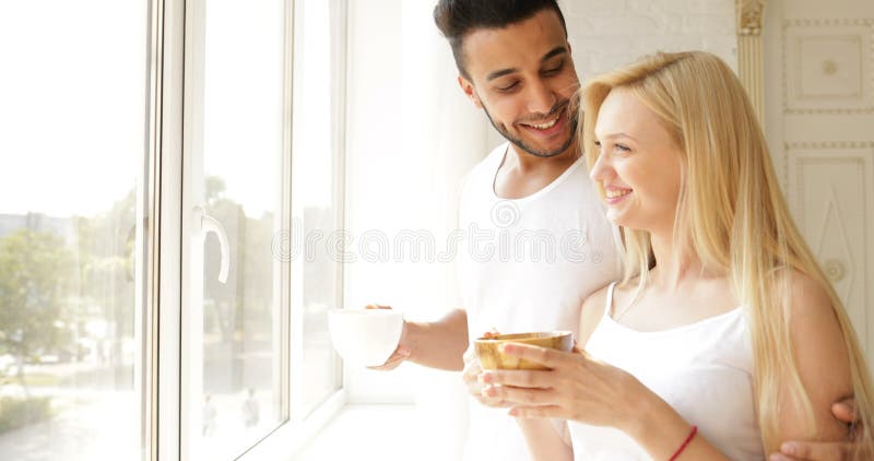 Το ζεύγος πίνει το πρωί καφέ κοντά στο χαμόγελο γυναικών ανδρών φυλών μιγμάτων παραθύρων απόθεμα βίντεο