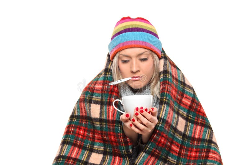 Ill woman covered with blanket holding a tea cup and a thermometer in her mouth isolated on white background. Ill woman covered with blanket holding a tea cup and a thermometer in her mouth isolated on white background