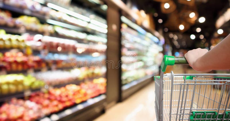 Το κάρρο αγορών υπεραγορών λαβής χεριών γυναικών με το αφηρημένο μανάβικο που θολώθηκε το υπόβαθρο στοκ φωτογραφία με δικαίωμα ελεύθερης χρήσης