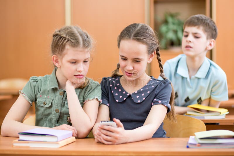 Το κορίτσι Schoolkid παρουσιάζει τηλέφωνο κυττάρων στους φίλους στοκ εικόνες Το κορίτσι Schoolkid παρουσιάζει τηλέφωνο κυττάρων στους φίλους στοκ εικόνες