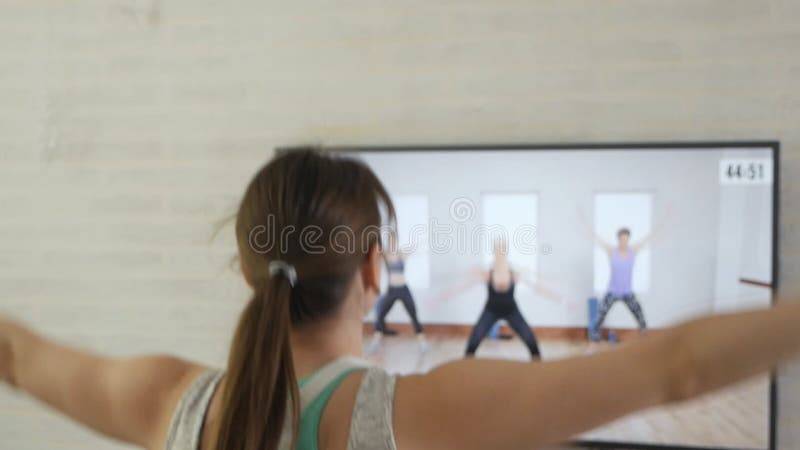 το κορίτσι κάνει ασκήσεις ενώ παρακολουθεί ένα πρόγραμμα στην τηλεόραση στο σπίτι. μια νεαρή γυναίκα με αθλητικό έργο αθλητικού αθ