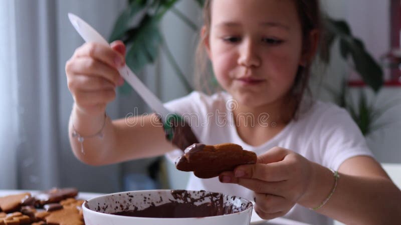 το κοριτσάκι κρατά το μπισκότο και εφαρμόζει παγωμένη σοκολάτα με βούρτσα