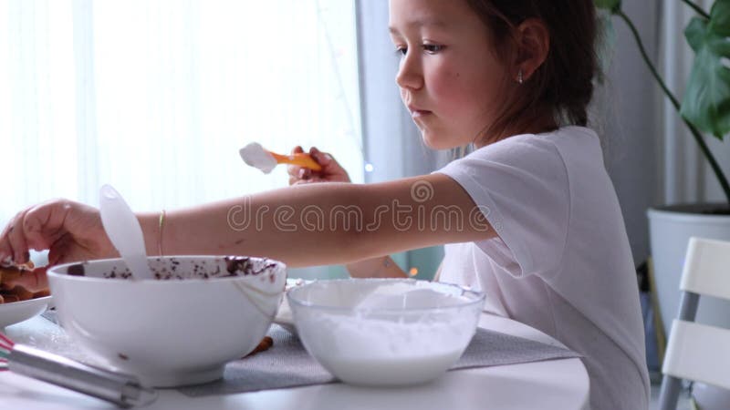 το κοριτσάκι κρατά το μπισκότο και εφαρμόζει παγωμένη σοκολάτα με βούρτσα