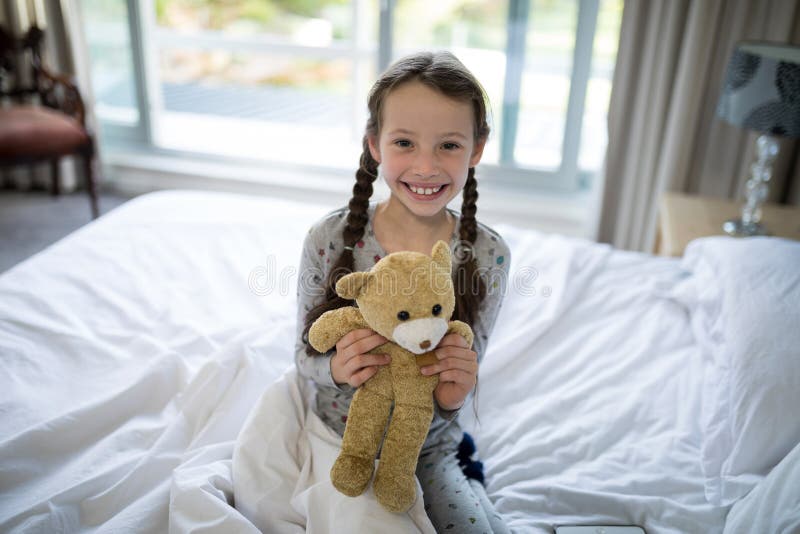 Το κράτημα κοριτσιών teddy αφορά το κρεβάτι στην κρεβατοκάμαρα στοκ εικόνα