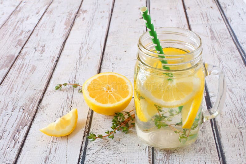 Lemon and thyme infused detox water in a mason jar glass against a rustic white wood background. Lemon and thyme infused detox water in a mason jar glass against a rustic white wood background