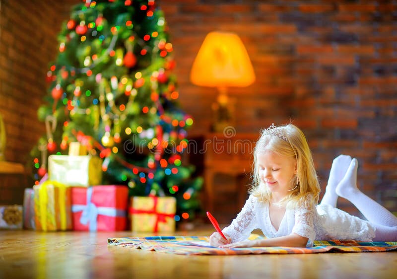Το μικρό κορίτσι γράφει μια επιστολή στο santa στο πάτωμα κοντά στο χριστουγεννιάτικο δέντρο στοκ φωτογραφίες με δικαίωμα ελεύθερης χρήσης Το μικρό κορίτσι γράφει μια επιστολή στο santa στο πάτωμα κοντά στο χριστουγεννιάτικο δέντρο στοκ φωτογραφίες με δικαίωμα ελεύθερης χρήσης