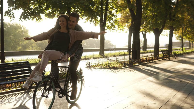 Το νέο ζεύγος έχει τη διασκέδαση οδηγώντας στο ίδιο ποδήλατο στην υπαίθρια δραστηριότητα με τον ήλιο backlight στο υπόβαθρο συνεδ
