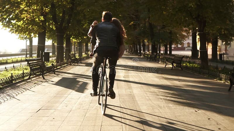 Το νέο ζεύγος έχει τη διασκέδαση οδηγώντας στο ίδιο ποδήλατο στην υπαίθρια δραστηριότητα με τον ήλιο backlight στο υπόβαθρο συνεδ